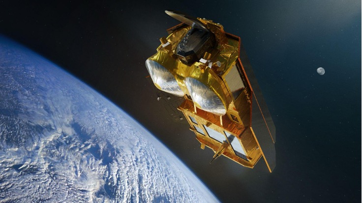 The image is an artist’s impression of a CRISTAL (Copernicus Polar Ice and Snow Topography Altimeter) satellite. The satellite features a rectangular main body covered in a golden insulating material, with large dual antennas at the front. It is depicted orbiting above the Earth, with the planet's icy surface visible below and the moon in the background. The satellite appears to be capturing data related to ice and snow topography. The background shows the dark expanse of space. This satellite image is credited to Airbus and the European Space Agency (ESA).