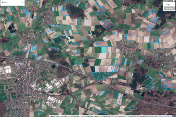 Aerial view of a colorful patchwork of agricultural fields marked with data overlays, alongside urban areas and roads.